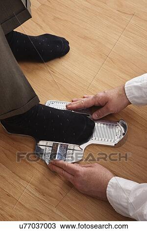 Stock Image - USA, Illinois, Metamora, Close up of sales clerk measuring man's foot at shoes store. Fotosearch