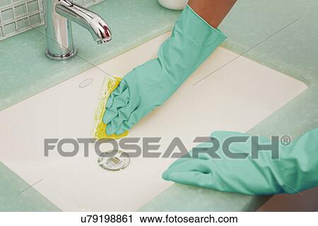 Stock Image - USA, Illinois, Metamora, Close-up of woman in rubber gloves cleaning bathroom sink. Fotosearch