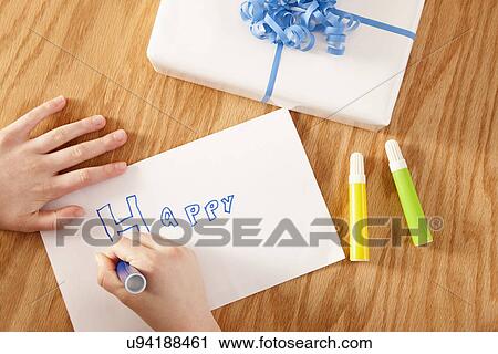 Stock Image - USA, Illinois, Metamora, Close-up of boy's (8-9) hands preparing greeting card and gift wrapped in paper. Fotosearch