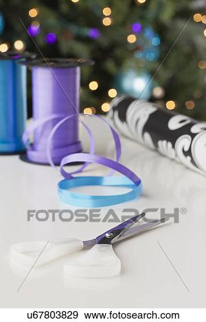 USA, Illinois, Metamora, Close-up of scissors, ribbon and wrapping paper on table, Christmas tree in background View Large Photo Image Stock Photo - USA, Illinois, Metamora, Close-up of scissors, ribbon and wrapping paper on table, Christmas tree in background. Fotosearch