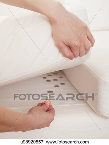 Stock Photo - USA, Illinois, Metamora, close-up of woman's hand hiding pennies under cushion. Fotosearch