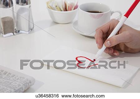 Stock Photograph - USA, Illinois, Metamora, Close-up of woman's hand drawing heart on napkin. Fotosearch