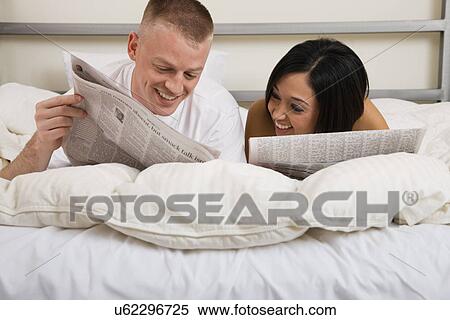 Stock Photography - USA, Illinois, Metamora, Couple lying in bed and reading newspaper. Fotosearch