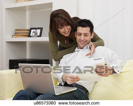 Stock Image - USA, Illinois, Metamora, Couple using laptop on sofa. Fotosearch