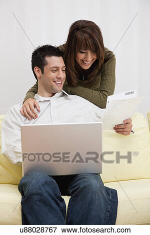 Stock Photo - USA, Illinois, Metamora, Couple using laptop on sofa. Fotosearch