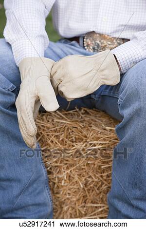 Stock Image - USA, Illinois, Metamora, Cowboy sitting on haystack, mid section. Fotosearch