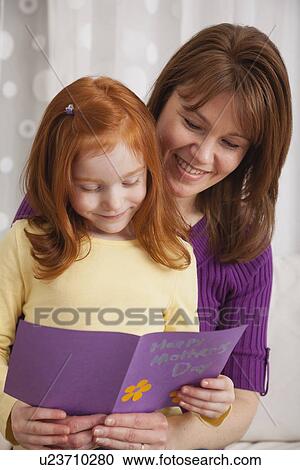 Stock Image - USA, Illinois, Metamora, Daughter (4-5) and mother reading greeting card for Mother's day. Fotosearch