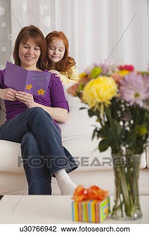 Stock Image - USA, Illinois, Metamora, Daughter (4-5) and mother reading greeting card for Mother's day. Fotosearch