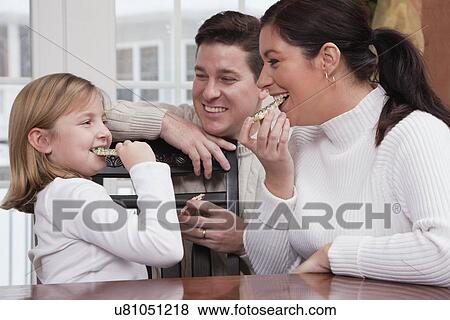 Stock Photo - USA, Illinois, Metamora, daughter (6-7), father and mother eating Christmas cakes. Fotosearch