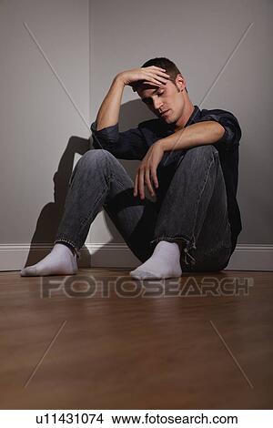 Picture - USA, Illinois, Metamora, Depressed man sitting on floor in empty room. Fotosearch