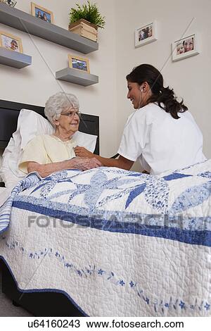 Stock Image - USA, Illinois, Metamora, Doctor examining senior woman sitting in bed. Fotosearch