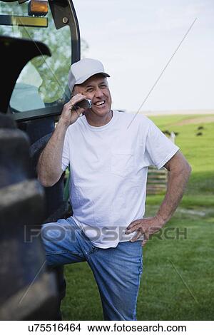 Picture - USA, Illinois, Metamora, Farmer using mobile phone by tractor in field. Fotosearch