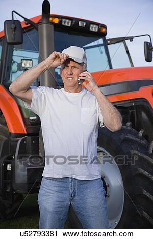 Stock Image - USA, Illinois, Metamora, Farmer using mobile phone by tractor. Fotosearch