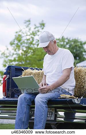 Stock Photo - USA, Illinois, Metamora, Farmer using laptop on truck. Fotosearch