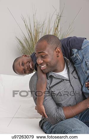 Stock Photo - USA, Illinois, Metamora, Father playing with son (6-7) on sofa. Fotosearch