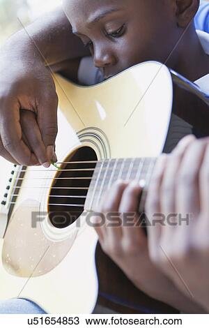 Stock Image - USA, Illinois, Metamora, Fathers and son (6-7) playing guitar. Fotosearch