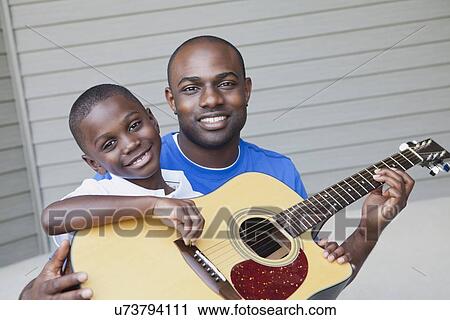 Stock Image - USA, Illinois, Metamora, Fathers and son (6-7) playing guitar. Fotosearch