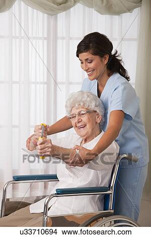 Picture - USA, Illinois, Metamora, Female nurse assisting senior woman on wheelchair using exercise band. Fotosearch