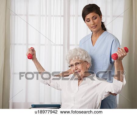 Stock Image - USA, Illinois, Metamora, Female nurse assisting senior woman using hand weights. Fotosearch