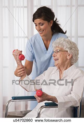 Stock Image - USA, Illinois, Metamora, Female nurse assisting senior woman using hand weights. Fotosearch