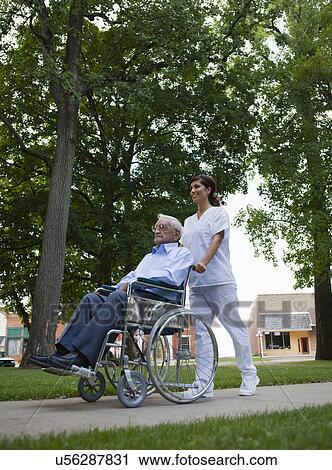 Stock Image - USA, Illinois, Metamora, Female nurse pushing senior man on wheelchair in park. Fotosearch