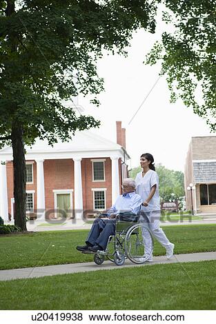 Stock Photo - USA, Illinois, Metamora, Female nurse pushing senior man on wheelchair in park. Fotosearch