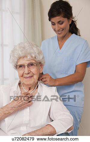 Stock Photo - USA, Illinois, Metamora, Female nurse helping senior woman to put pearl necklace. Fotosearch
