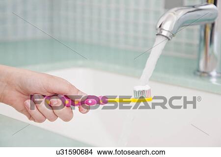 Picture - USA, Illinois, Metamora, girl (10-11) holding toothbrush under tap. Fotosearch