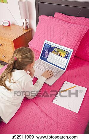 Stock Photo - USA, Illinois, Metamora, Girl (10-11) with laptop lying on bed. Fotosearch