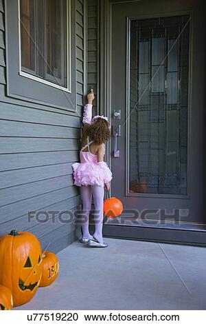 Stock Image - USA, Illinois, Metamora, Girl (6-7) in Halloween costume knocking to doors. Fotosearch