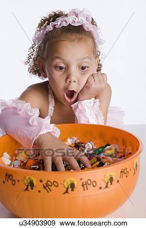 USA, Illinois, Metamora, Girl (6-7) in costume taking candies from bowl and making face View Large Photo Image Stock Photo - USA, Illinois, Metamora, Girl (6-7) in costume taking candies from bowl and making face. Fotosearch