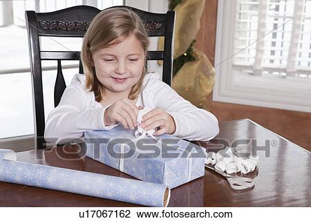Stock Image - USA, Illinois, Metamora, girl (6-7) wrapping Christmas present. Fotosearch