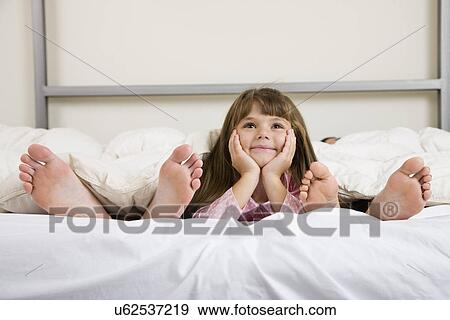 USA, Illinois, Metamora, Girl (6-7) lying on bed near parent's feet View Large Photo Image Stock Photo - USA, Illinois, Metamora, Girl (6-7) lying on bed near parent's feet. Fotosearch