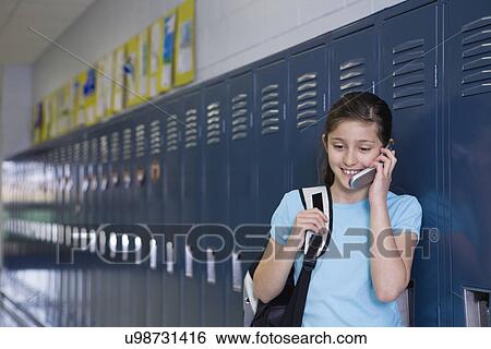 Stock Photograph - USA, Illinois, Metamora, Girl (8-9) standing at lockers in school corridor and talking on mobile phone. Fotosearch