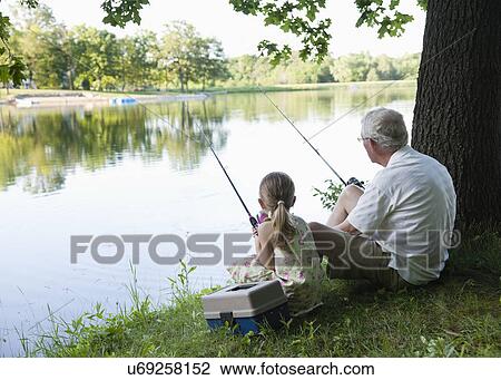 Stock Image - USA, Illinois, Metamora, grandfather and granddaughter (4-5) sitting at edge of lake. Fotosearch