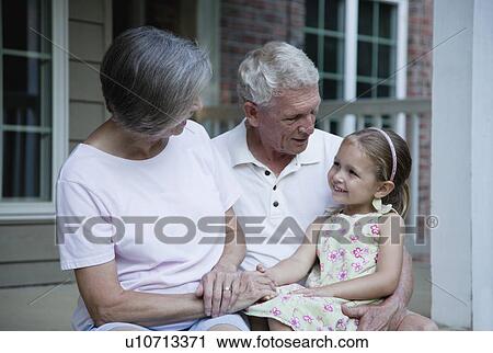 Stock Image - USA, Illinois, Metamora, grandparents and granddaughter (4-5) sitting in front of house. Fotosearch