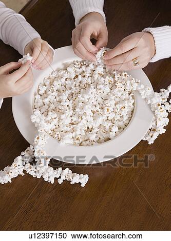 Stock Image - USA, Illinois, Metamora, hands of mother and daughter (6-7) making popcorn Christmas ornament. Fotosearch