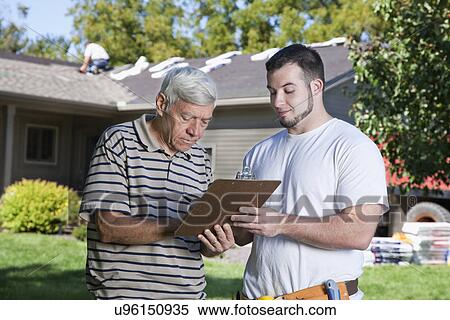 Stock Photography - USA, Illinois, Metamora, Home owner signing bill from construction worker. Fotosearch