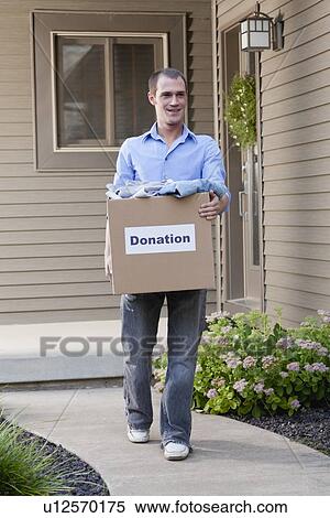 Stock Photography - USA, Illinois, Metamora, Man carrying cardboard box in front of house. Fotosearch