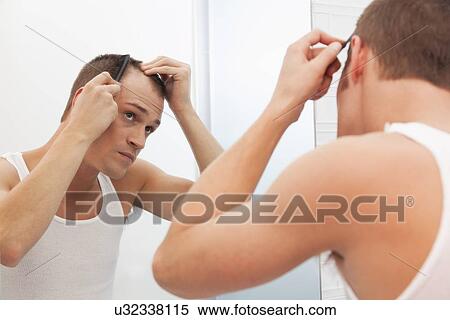 Stock Photography - USA, Illinois, Metamora, Man combing hair in front of mirror. Fotosearch