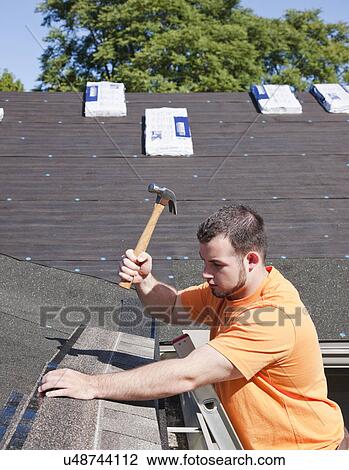 Stock Image - USA, Illinois, Metamora, Man hammering shingles onto roof. Fotosearch
