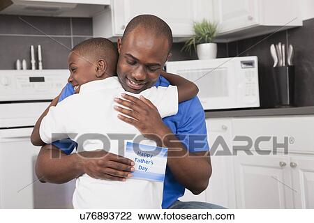 Stock Image - USA, Illinois, Metamora, Man holding father's day card and embracing son (6-7). Fotosearch