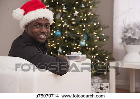 USA, Illinois, Metamora, Man in Santa hat sitting on sofa near Christmas tree View Large Photo Image Picture - USA, Illinois, Metamora, Man in Santa hat sitting on sofa near Christmas tree. Fotosearch