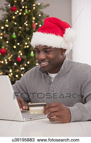 Stock Image - USA, Illinois, Metamora, Man in Santa hat using laptop. Fotosearch