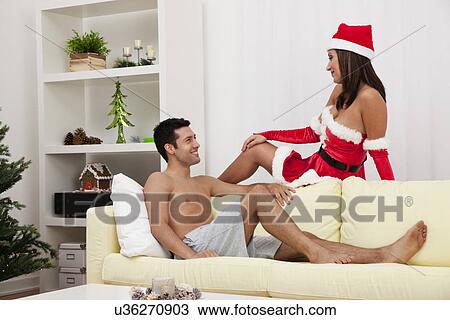 Stock Image - USA, Illinois, Metamora, Man looking at woman wearing Santa hat in living room. Fotosearch