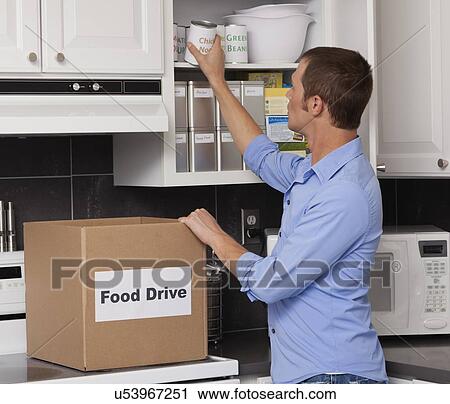 Stock Image - USA, Illinois, Metamora, Man placing canned food in kitchen cupboard. Fotosearch