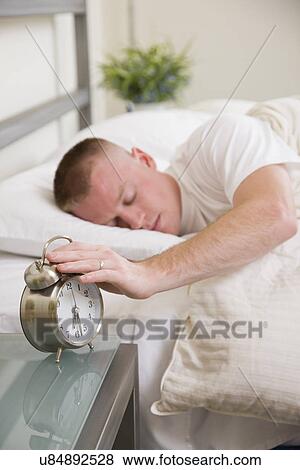 Stock Photo - USA, Illinois, Metamora, Man sleeping with hand on alarm clock. Fotosearch