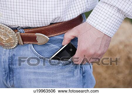 Stock Photograph - USA, Illinois, Metamora, Man wearing jeans and ornate belt holding mobile phone, mid section. Fotosearch