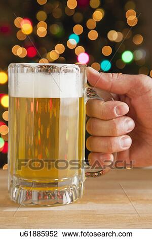 Stock Image - USA, Illinois, Metamora, Man's hand holding beer, Christmas lights in background. Fotosearch