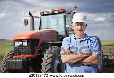 Stock Image - USA, Illinois, Metamora, mature farer standing in front of tractor on field. Fotosearch
